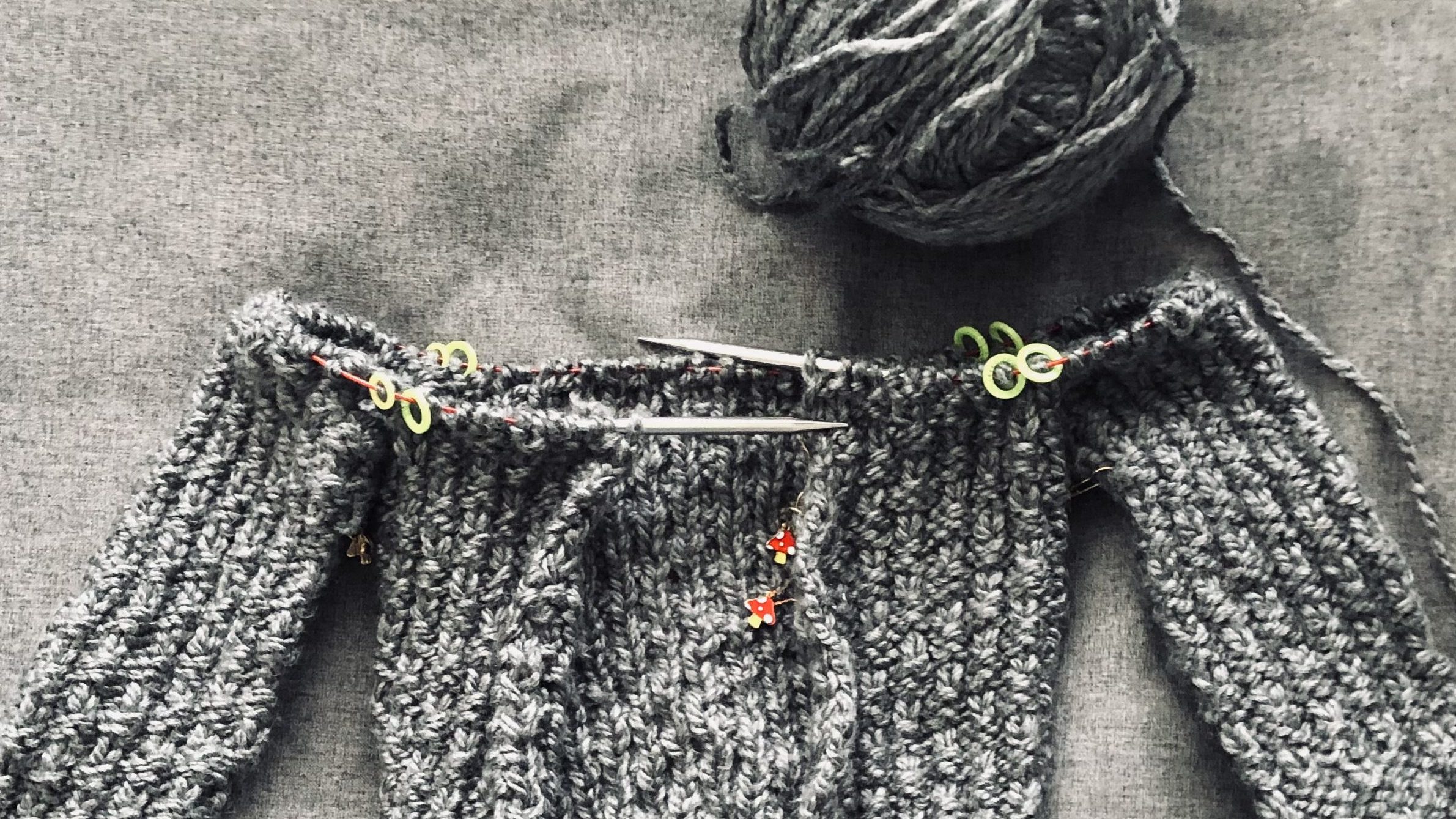 Grey handmade knitted sweater called the Oxbow Cardigan on knitting needles